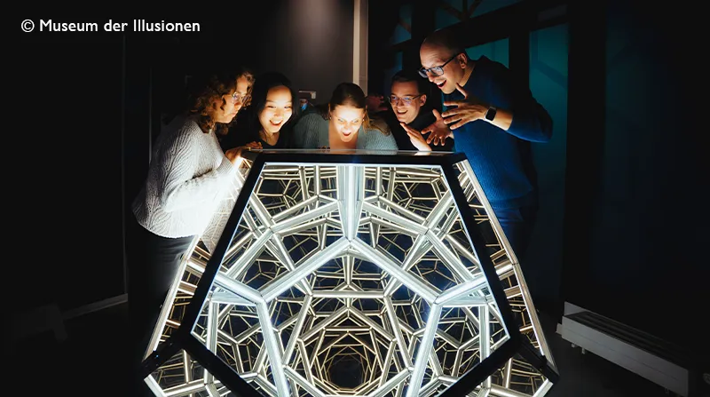 Besucher betrachten eine leuchtende Spiegelillusion im Museum der Illusionen